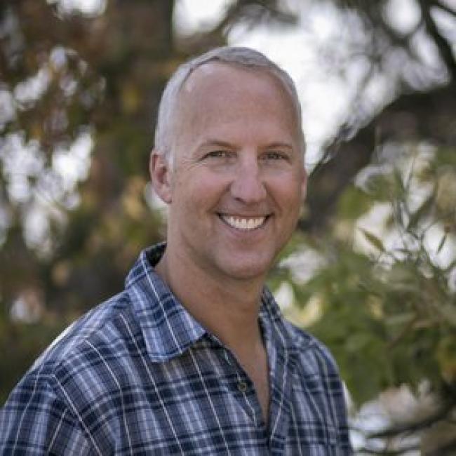 Headshot of Joe Gaydos. He is looking at the camera and smiling. There are trees blurred in the background.