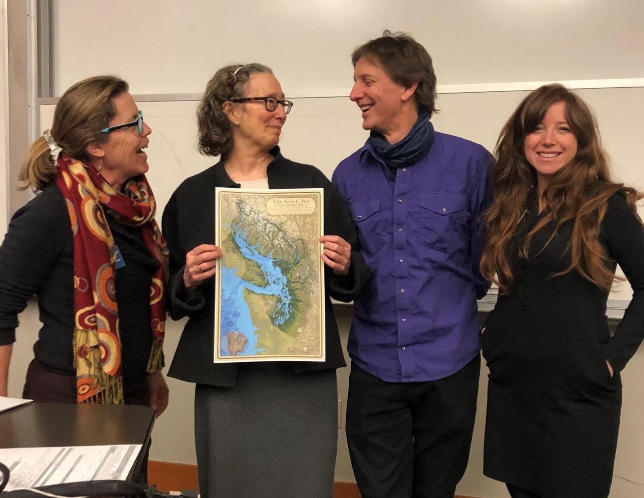 Lynda Mapes and Stefan Freelan exchanging smiles while Lynda holds the Salish Sea map that Stefan created. Also in the picture is Ginny Broadhurst and Natalie Baloy.